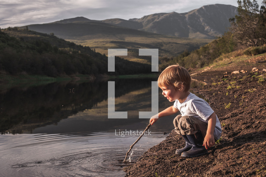 a toddler boy playing with a stick in a pond 