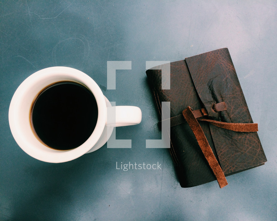 A cup of coffee next to a leather journal.