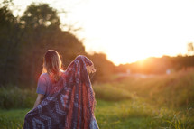 a woman wrapped in a blanket standing outdoors at sunset 