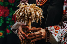Ukrainian woman in traditional costume with bouquet Didukh on colorful bukovyna ornaments carpet. Christmas decoration, made from sheaf of wheat. 