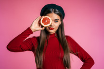 Portrait of young beautiful woman in red with two half of juicy grapefruit on pink studio background. Healthy eating, dieting, antioxidants concept