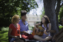 women playing music and reading Bibles on a blanket in a park 