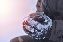 male hand in gloves holding cup with hot tea or coffee. Tea break. Winter time concept
