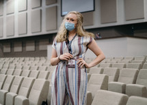 a woman in a mask standing in an auditorium 