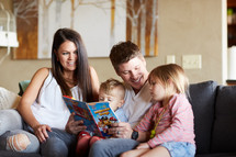 a mother and father reading a book to their kids 