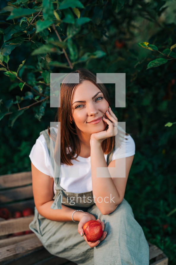 Woman with red juicy apple from tree in own home countryside orchard. Happy gardener, young farmer style. Healthy lifestyle. High quality