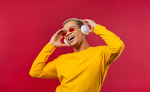 Positive man listening music, enjoying dance with headphones on red studio background. 