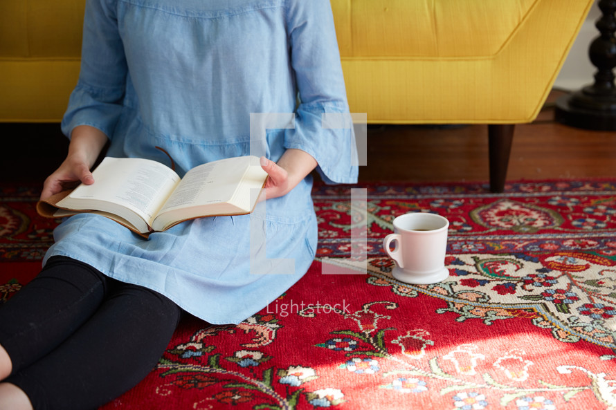 a woman sitting on a rug reading a Bible 