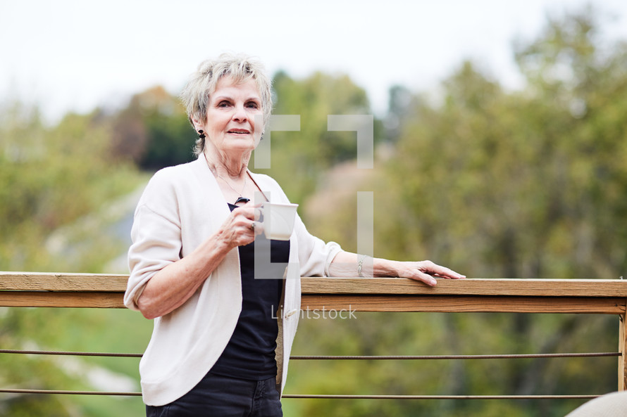 an elderly woman standing by a railing with coffee