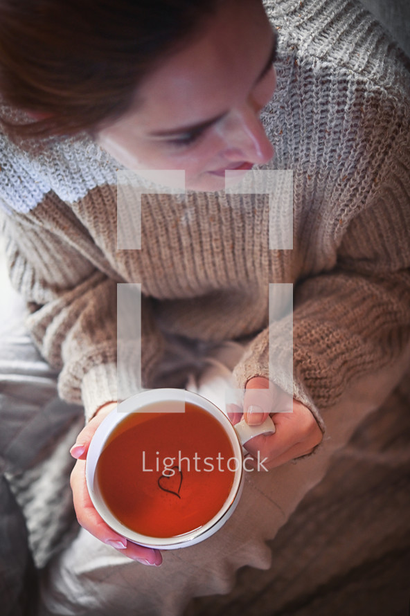 Woman holding mug of tea with heart in the bottom