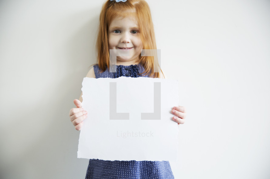 A little girl holds up a blank piece of paper.