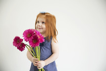 A little girl holds a bouquet of pink flowers.