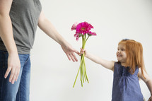 A little girl hands her mother a bouquet of pink flowers.
