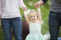 a toddler swinging holding mother and father's hands 