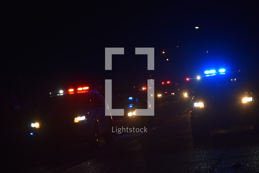 A line of approaching police cars with lights flashing at night 