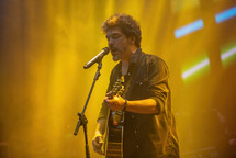 Man singing and playing guitar at a concert 