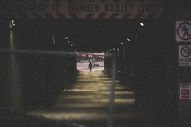 man walking under a bridge and a chain linked fence 