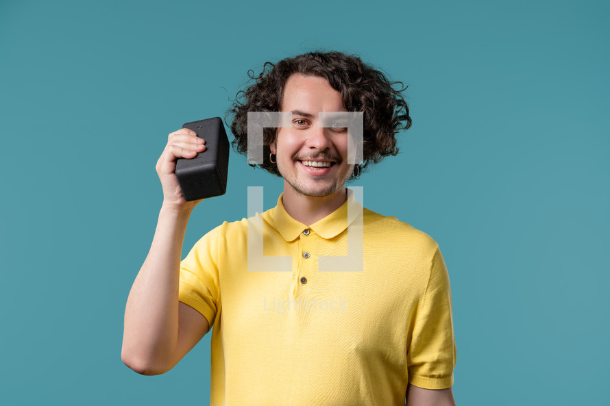 Man dancing, enjoying on blue studio background. Guy moves to rhythm of music. Young dude listening to music by wireless portable speaker - modern sound system. High quality