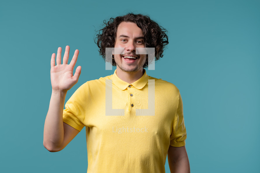 Friendly young man waving hand - hello, or goodbye, chao, salute. Parting, say bye to camera. Handsome man on blue studio background. High quality photo