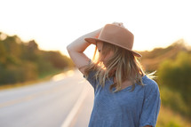 a woman in a hat standing on the side of the road 