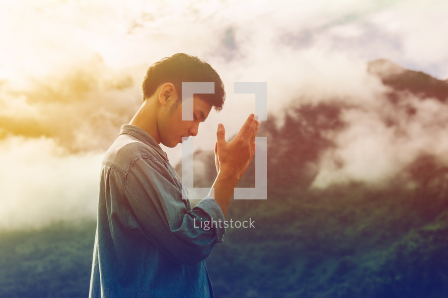 man with raised hands praying outdoors 