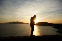 a man praying on a shore at sunset  