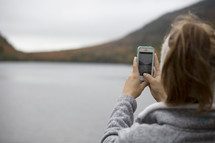 woman taking a picture of a lake with her cellphone 