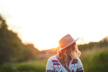 woman in a hat and sweater standing outdoors in sunlight 