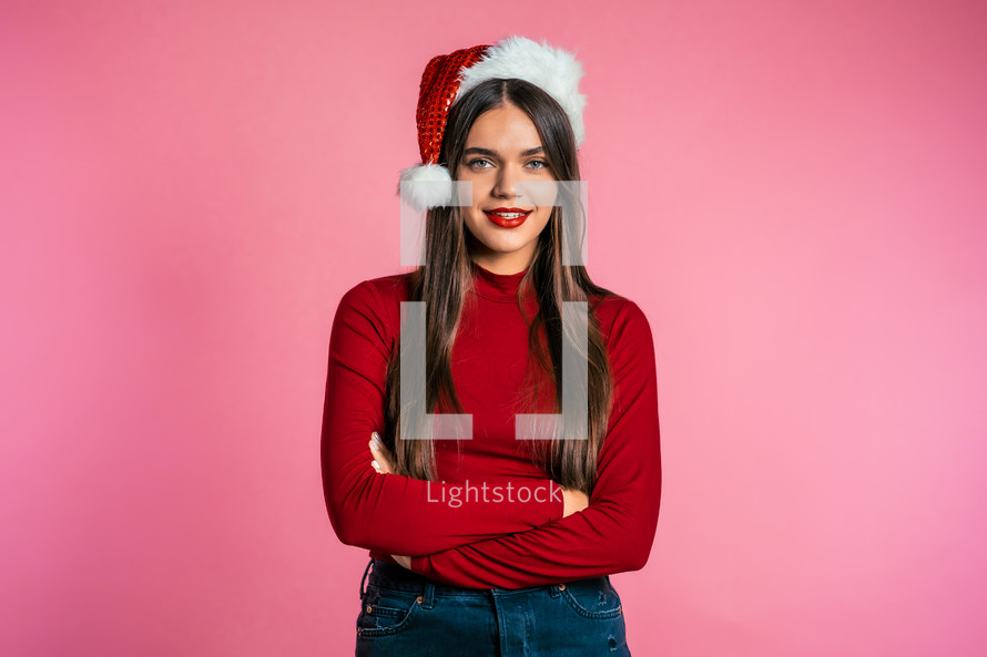 Attractive girl in Santa hat. Portrait of lady on pink background. Christmas or New year concept. Happy pretty woman smiling to camera