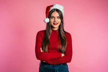 Attractive girl in Santa hat. Portrait of lady on pink background. Christmas or New year concept. Happy pretty woman smiling to camera