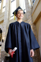 teen boy in his cap and gown holding his diploma 