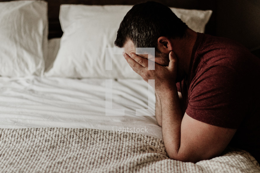 a man kneeling in prayer over a bed covering his face 