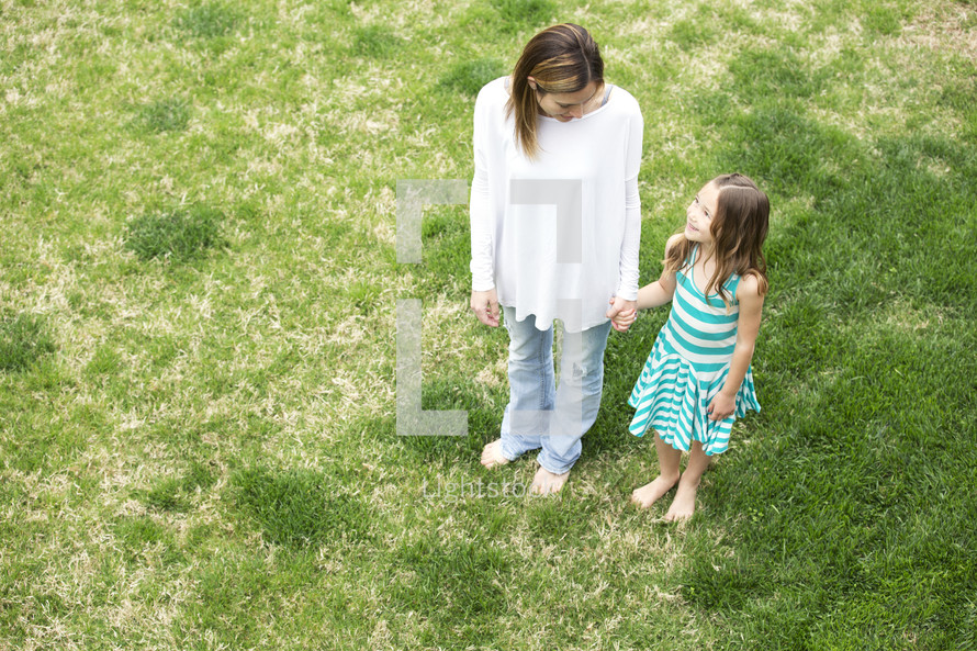a mother and daughter holding hands standing in grass 