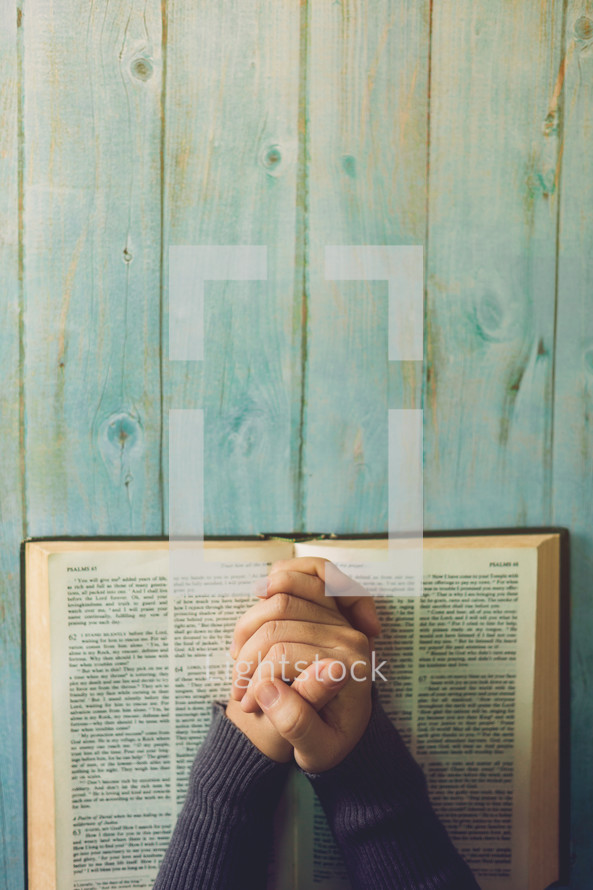 praying hands over the pages of a Bible 