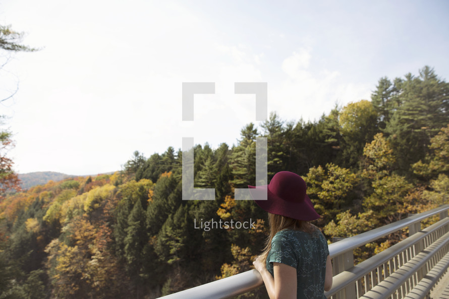 woman looking over a railing at a mountain fall forest 
