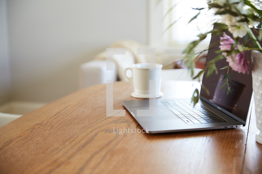 flowers in a vase, coffee cup, and laptop computer on a desk 