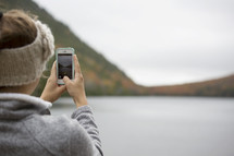 woman taking a picture of a lake with her cellphone 