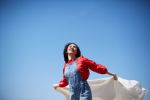a woman with outstretched arms holding a white sheet and looking up