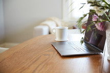 flowers in a vase, coffee cup, and laptop computer on a desk 