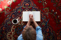 a woman praying over a Bible sitting on a rug 