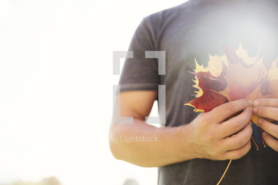 a man holding a hand full of fall leaves 