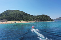 Small boat with tourists heading to iconic small uninhabited island of Marathonisi featuring clear water sandy shore and natural hatchery of Caretta-Caretta sea turtles, Zakynthos island, Ionian, Greece
