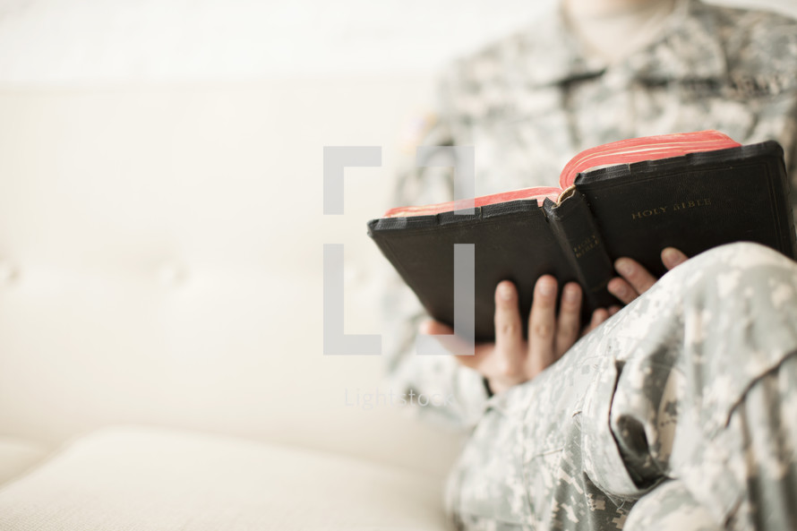 Female soldier in uniform sitting on a sofa reading a Bible.