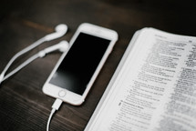iPhone with earbuds and an open Bible 