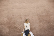 a woman holding shopping bags against a brick wall.