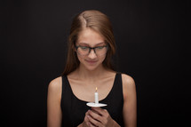 a girl holding a candle with head bowed 