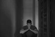 a man sitting in a dark hallway covering his face 