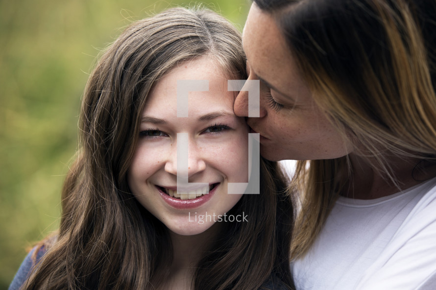 a mother kissing her teenage daughter on the cheek 
