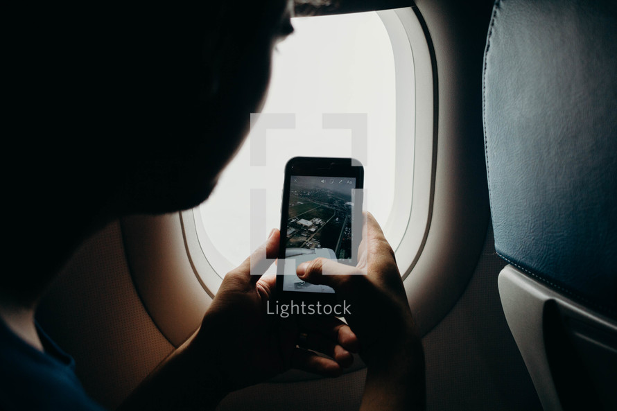 boy taking a picture with his cellphone from an airplane 