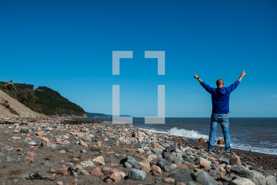 man standing on a shore with raised hands 